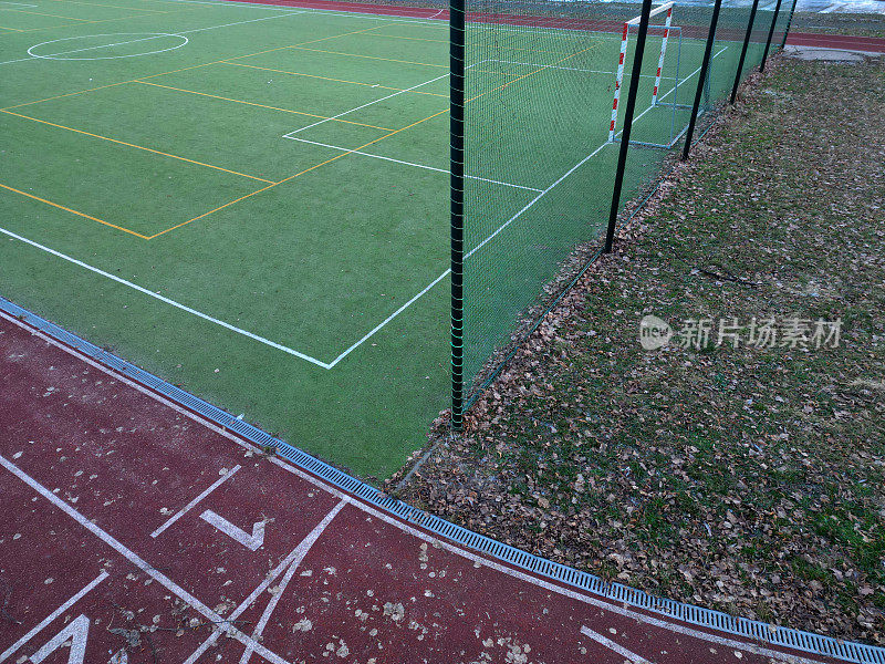 sports stadium with a running track with several lanes. inside oval there is a small football field for netball and handball with shield barriers. synthetic turf. view from top, all weather track